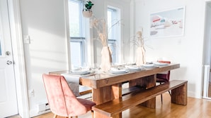 Un comedor con una mesa de madera dispuesta para cuatro, una silla rosa y un banco.