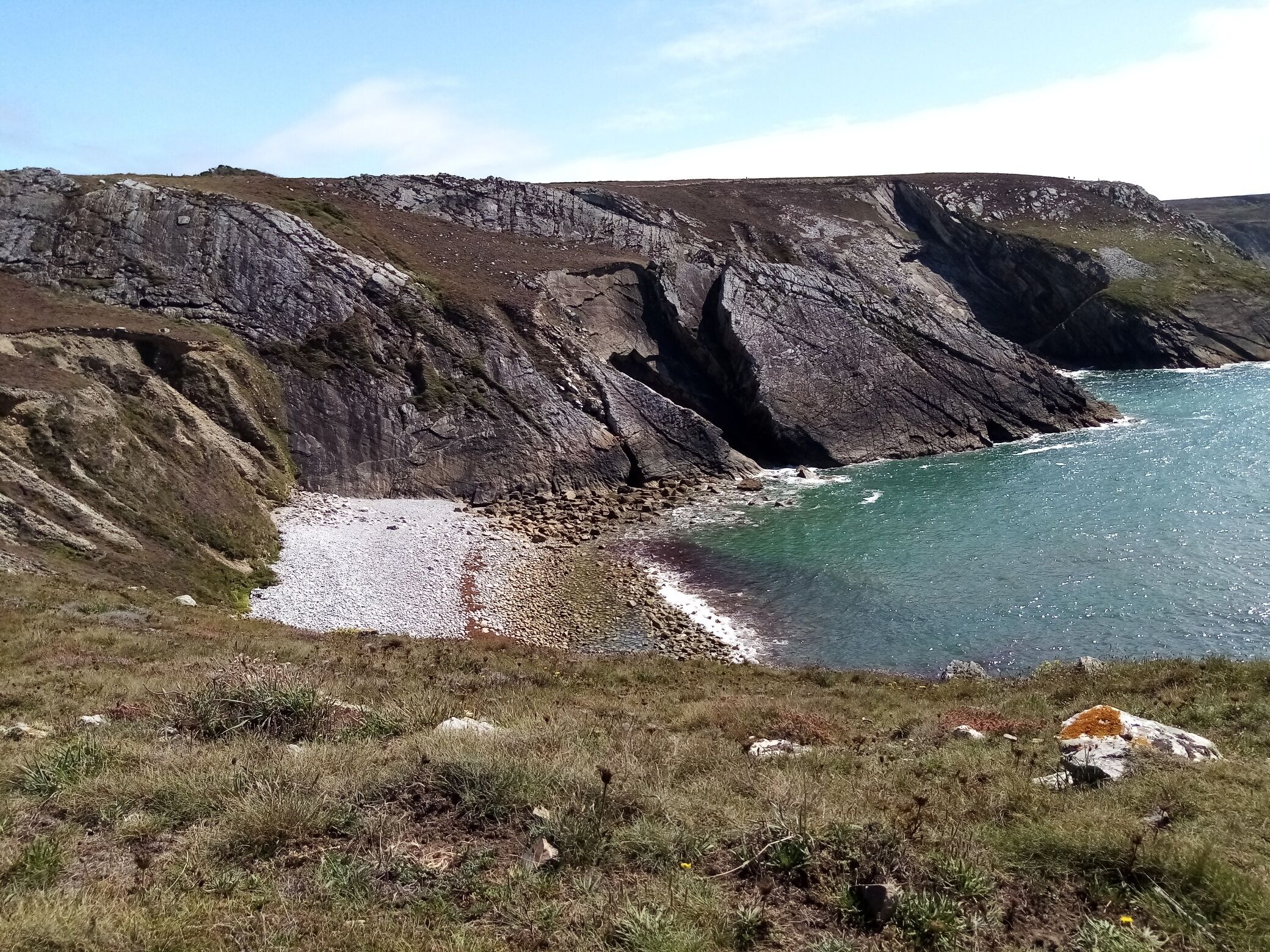 Paisagem costeira com falésias rochosas e uma praia de pedrinhas.