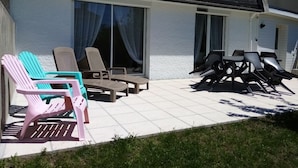 Un patio con mesas al aire libre y un edificio de amplios ventanales y techo oscuro.