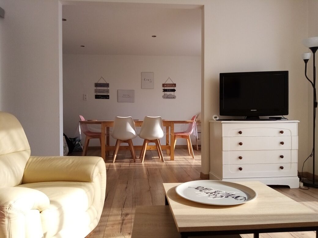 A living room with a sofa, a dining table with chairs, a TV on a stand, and a cabinet.