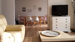 Una sala de estar con un sofá, una mesa de comedor con sillas, un televisor sobre un mueble bajo y un aparador.