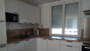 Una cocina moderna con armarios blancos, un microondas integrado, una cafetera y una ventana con persianas.