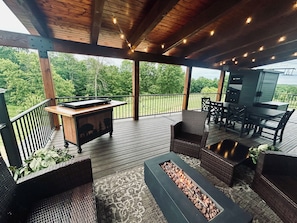 Een overdekt terras buiten met een barbecuehoek, zitplaatsen en uitzicht op de omliggende groene omgeving.