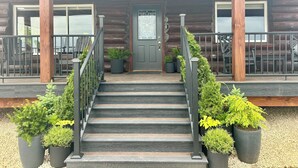 A wooden cabin with a front porch, steps leading to a door, and potted plants. - Secluded cabin on 75 acres 360 views cedar hot tub infrared sauna outdoor Shower (Viola)