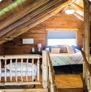 Een knus zolderkamer met een bed, een klein nachtkastje, een hanglamp en een raam met jaloezieën.