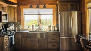 A rustic kitchen with wooden cabinets, a stainless steel refrigerator, and a large window with a view of the outdoors. - Secluded cabin on 75 acres 360 views cedar hot tub infrared sauna outdoor Shower (Viola)