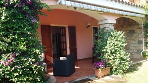 A covered outdoor seating area with wicker furniture, surrounded by lush greenery and potted plants. - Holidays at Hydrangea Villa (San Teodoro)