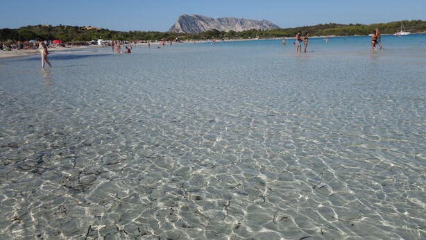 A beach with clear shallow water, people walking, and a mountain in the background. - Holidays at Hydrangea Villa (San Teodoro)