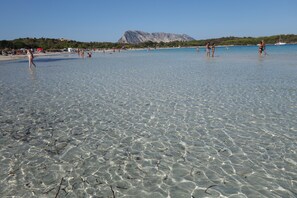 A beach with clear shallow water, people walking, and a mountain in the background. - Holidays at Hydrangea Villa (San Teodoro)