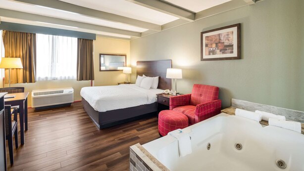 Une chambre d’hôtel avec un grand lit, un canapé séparé, un fauteuil rouge, un bureau et une grande baignoire.