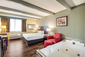 A hotel room with a large bed, a separate sofa, a red armchair, a desk, and a large bathtub. - Suburban Studios Buffalo Airport (Buffalo)