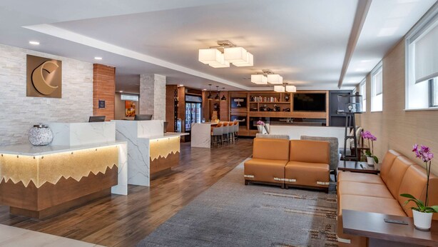 Un moderno vestíbulo de hotel con mostrador de recepción, zona de estar y cocina al fondo.