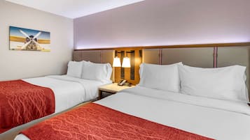 A hotel room with two beds, a nightstand with a lamp, and a painting of an airplane on the wall.