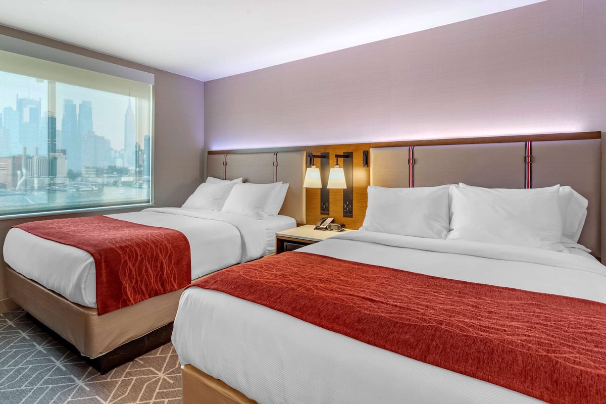 A hotel room with two beds, a city view, and a nightstand with a lamp.