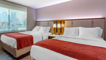 A hotel room with two beds, a city view, and a nightstand with a lamp.