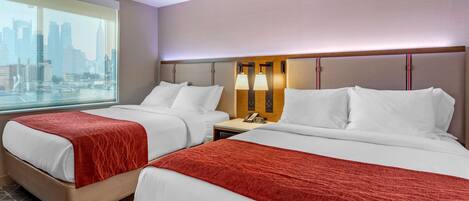 A hotel room with two beds, a city view, and a nightstand with a lamp.