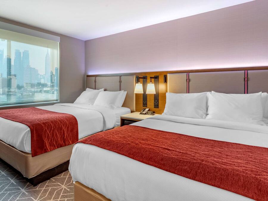A hotel room with two beds, a city view, and a nightstand with a lamp.