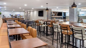 Un restaurante moderno con mesas comunitarias largas y cabinas, una zona de bar y una cocina visible al fondo.