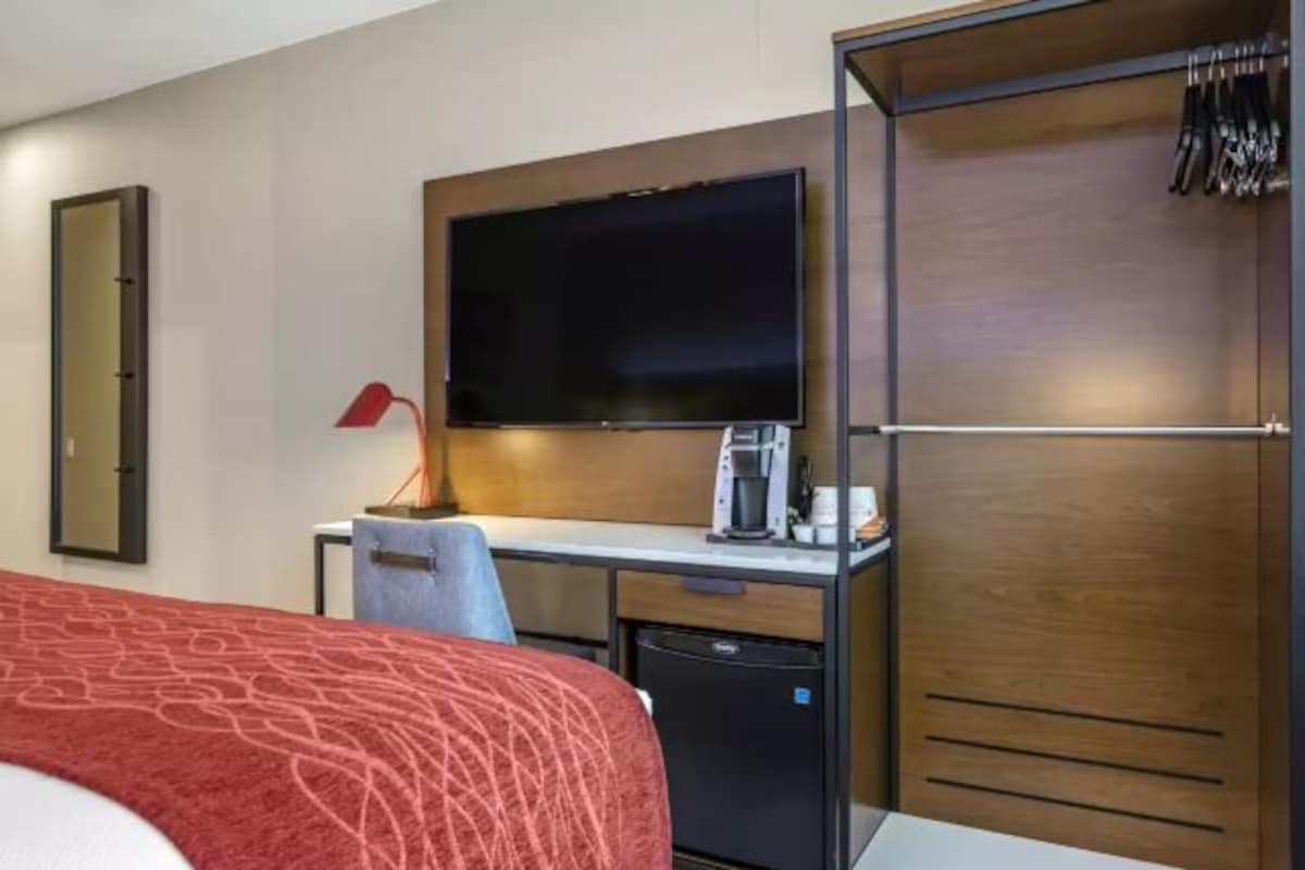 A hotel room with a bed, a desk with a flat-screen TV, a coffee maker, and a wardrobe.