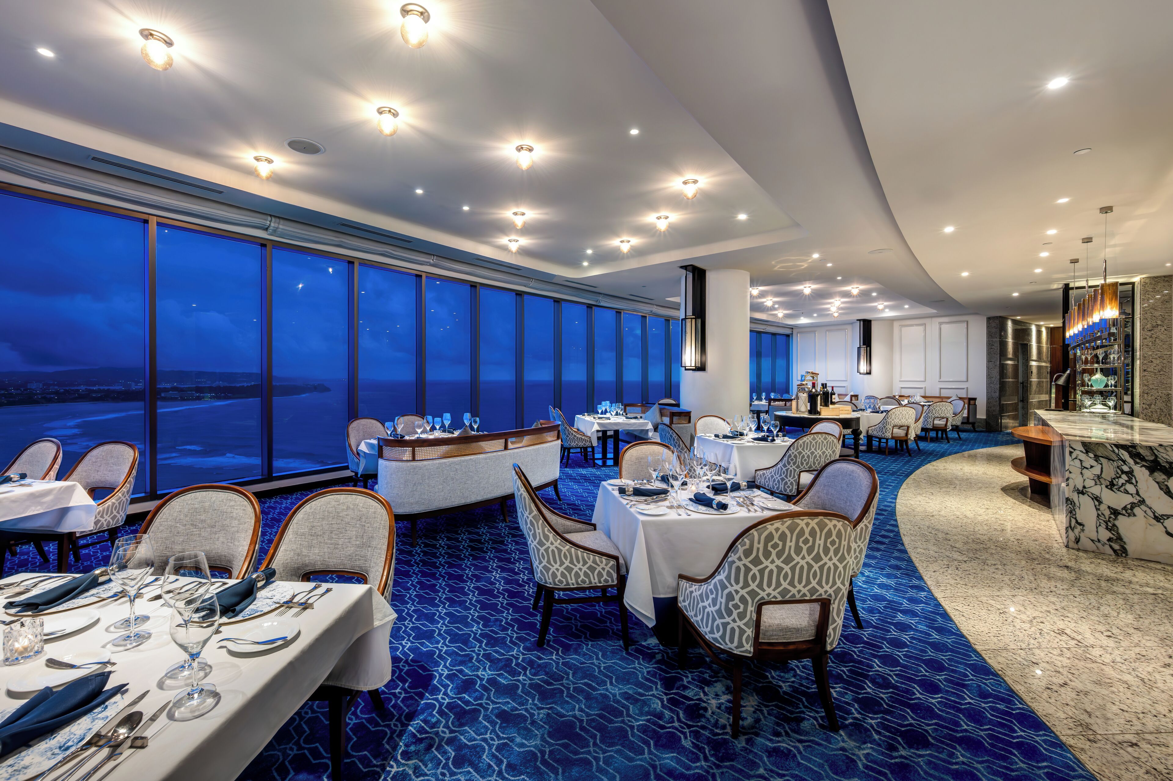 Comedor con mesas dispuestas para el servicio, ventanas amplias y vista al cielo nocturno.