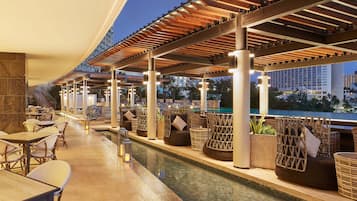 A rooftop bar with outdoor seating, a pool, and a view of the city skyline.