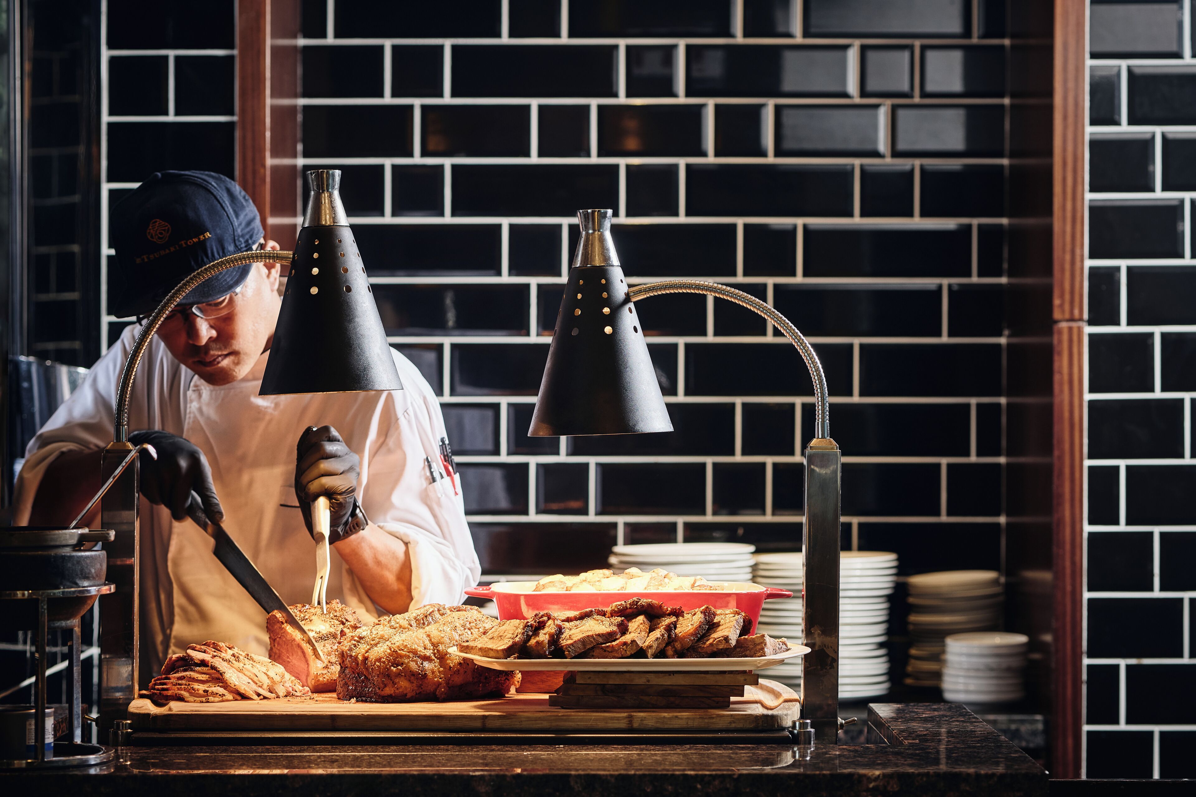 A person slicing meat on a cutting board with a knife, a hookah, and a lamp in a kitchen setting.