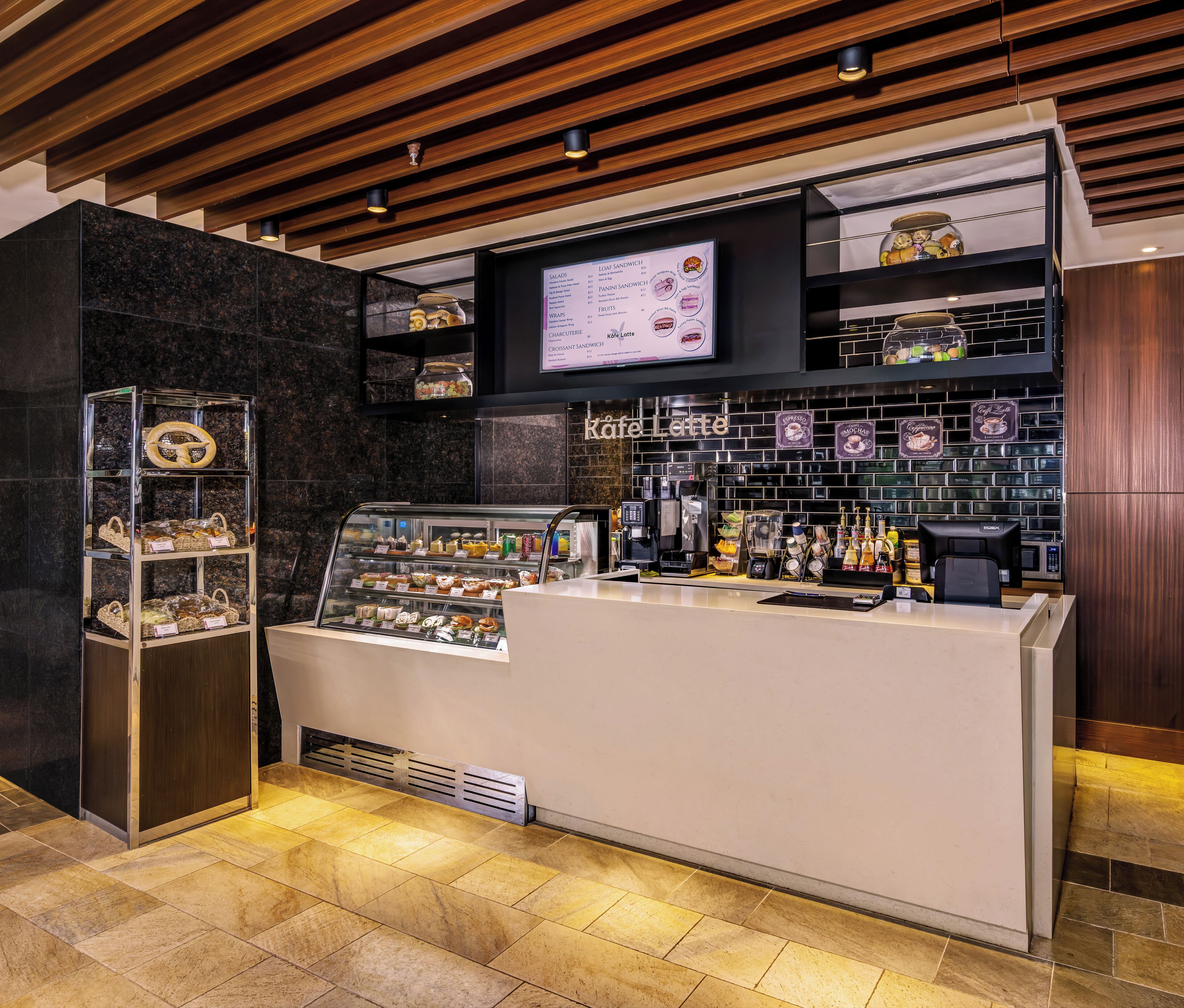 Mostrador de cafetería con una pantalla de menú, una caja registradora y una variedad de café y productos de pastelería.