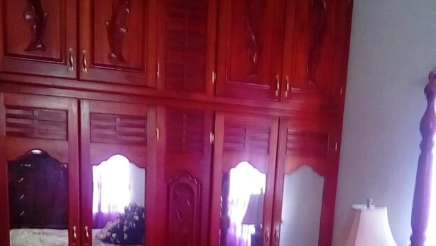 A bedroom with a large wardrobe, a bed with a purple and white bedspread, and a bedside lamp. - Agatha's Home In Paradise  (Westmoreland Parish)