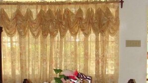 A dining room with a long table, chairs, a chandelier, and a curtain. - Agatha's Home In Paradise  (Westmoreland Parish)
