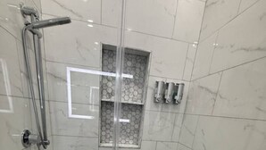Une douche fermée par des parois en verre, dotée d’un sol carrelé avec des motifs hexagonaux, d’une barre d’appui et d’une petite fenêtre ornée d’un motif hexagonal.