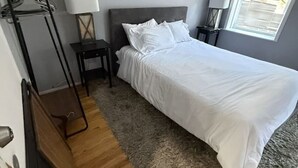 Une chambre à coucher avec un lit, une table de chevet, une lampe, un tableau et une fenêtre.