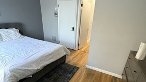 Une chambre à coucher avec un lit, un tapis foncé, un plancher en bois, une porte blanche et un mur gris.