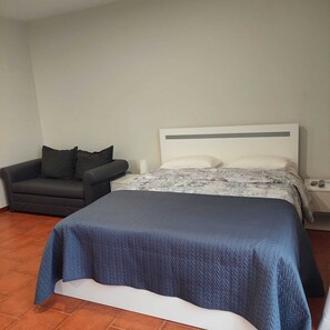 A bedroom with a bed, a chair, and a nightstand.