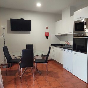 A compact kitchen with a dining area, white cabinets, a microwave, oven, and a flat-screen TV.