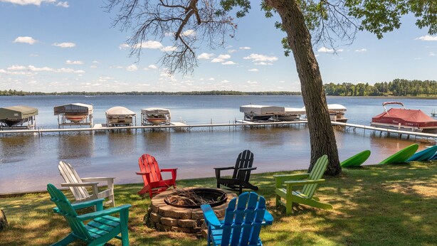 A lakeside deck with Adirondack chairs, a fire pit, and canopies over boats. - Cabin on Farm Island Lake in Aitkin (Aitkin)