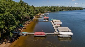 A docked boat marina with several boats covered with tarps, surrounded by dense forest. - Cabin on Farm Island Lake in Aitkin (Aitkin)