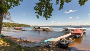 A lakeside dock with boats and canopies, surrounded by trees and a clear sky. - Cabin on Farm Island Lake in Aitkin (Aitkin)