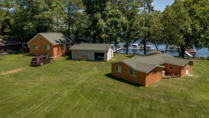A log cabin with a garage, a small shed, and a car parked in a grassy yard. - Cabin on Farm Island Lake in Aitkin (Aitkin)