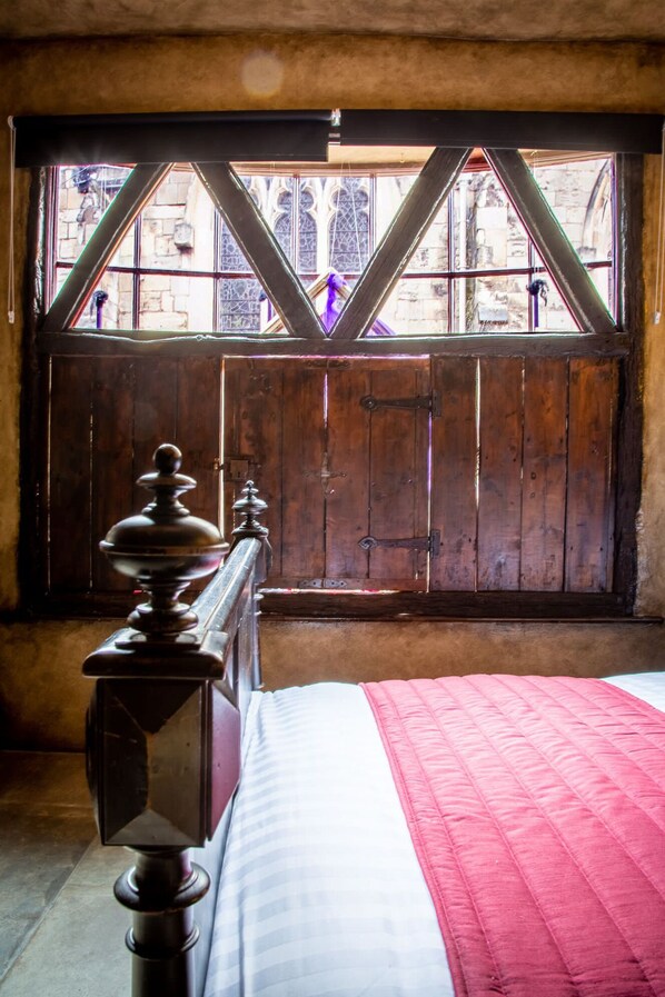 A room with a wooden bed, a window with a view of buildings, and a red blanket on the bed.