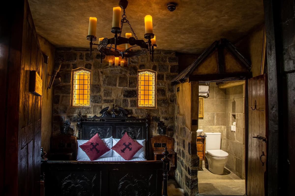 A rustic bathroom with stone walls, a wooden door, a white toilet, and a chandelier with candles.