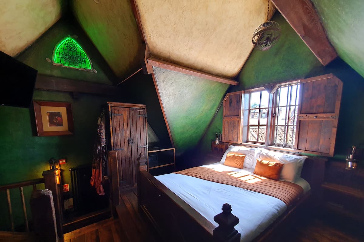 A bedroom with a wooden bed, a green wall, and a window with wooden shutters.