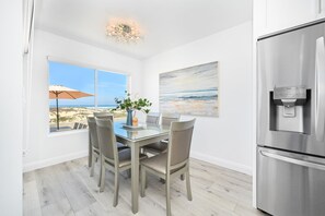 Eine moderne Küche mit einem Edelstahl-Kühlschrank, einem Esstisch mit vier Stühlen, einem Wasserspender und einem großen Fenster mit Blick auf den Strand.