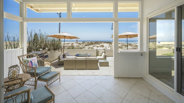 A sunlit patio with wicker furniture, two umbrellas, and a view of the beach. - BRAND NEW LOWER UNIT ON BEACH W/ PATIO & FIREPIT (Newport Beach)