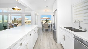 A modern kitchen with white cabinetry, a large island, and a view of the beach. - BRAND NEW LOWER UNIT ON BEACH W/ PATIO & FIREPIT (Newport Beach)