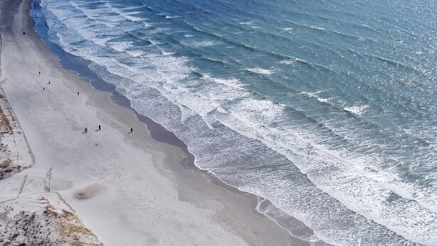 Ein Strand mit brechenden Wellen, einem klaren Himmel und einer fernen Küstenlinie.