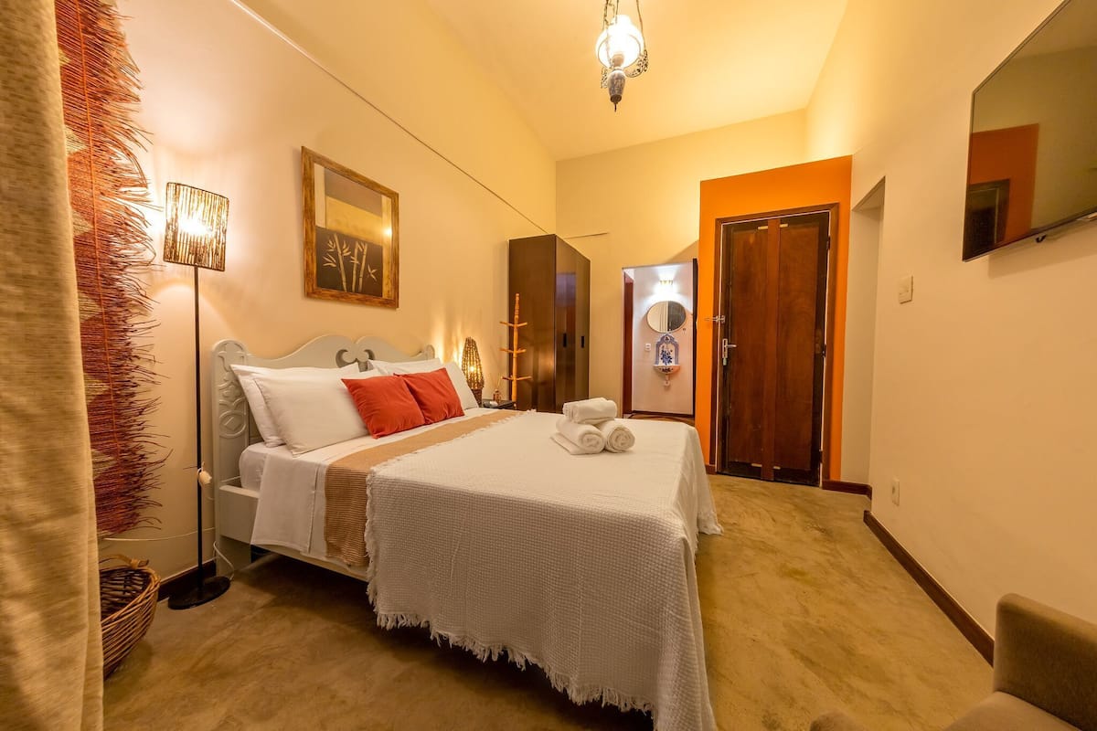 A hotel room with a bed, a bedside lamp, a wall clock, a mirror, and a door.