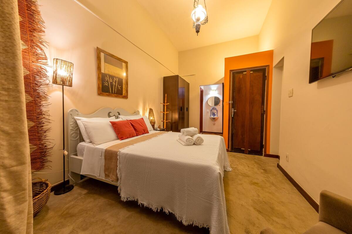A hotel room with a bed, a bedside table, a lamp, a mirror, and a door.