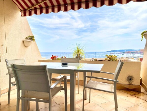 Une terrasse avec une table et des chaises, une vue sur la mer et un auvent rayé de rouge et de blanc.