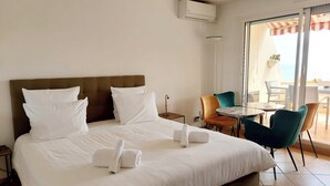 Ein Hotelzimmer mit Bett, kleinem Tisch, Stühlen, Deckenventilator und Blick ins Freie.