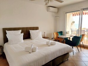 Hotellihuone, jossa on sänky, pieni pöytä, tuoleja, kattotuuletin ja näkymä ulos.